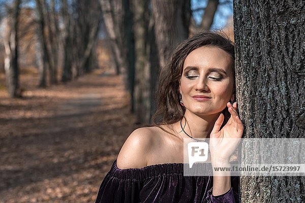 Girl in a dark dress on a linden alley in an autumn day.