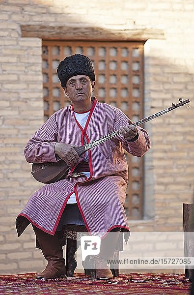 Mann in Tracht spielt auf der Dombra  einem traditionellen Zupfinstrument  Altstadt von Chiwa  Provinz Xorazm  Usbekistan  Asien