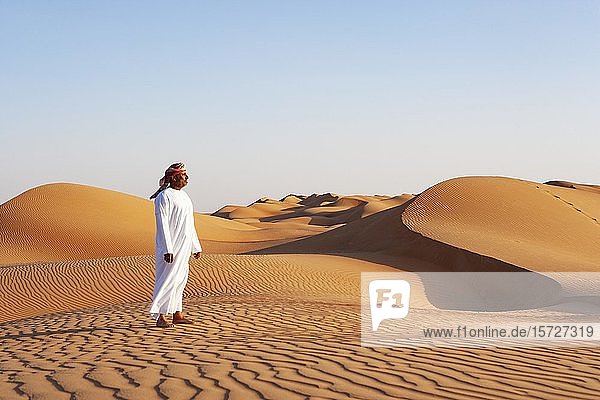 Beduine in traditioneller Kleidung steht in der Sandwüste  Sanddünen  Wüste Rimal Wahiba Sands  Oman  Asien