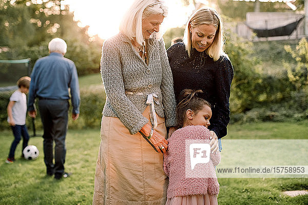 Girl embracing with mother and grandmother while standing in backyard