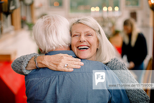 Porträt einer älteren Frau  die einen Mann umarmt  während sie zu Hause steht