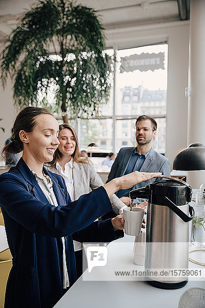 Lächelnde Kollegen sehen Geschäftsfrau in der Pause beim Kaffee trinken an