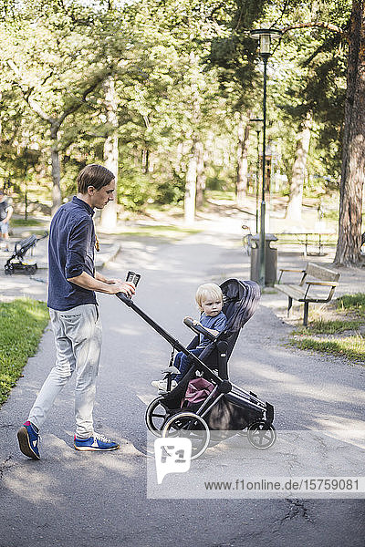 Mann läuft in voller Länge  während er seinen Sohn im Kinderwagen im öffentlichen Park schiebt