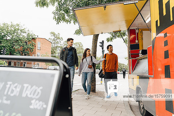 Full length of friends walking on street by food truck in city