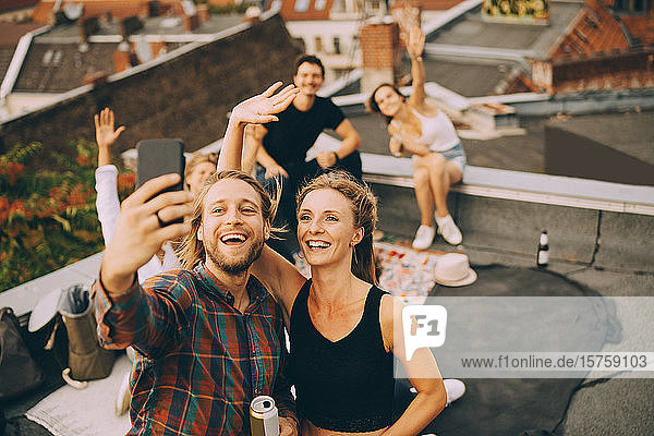 Fröhlicher Mann nimmt Selfie mit Freunden am Smartphone mit  während er auf der Terrasse feiert
