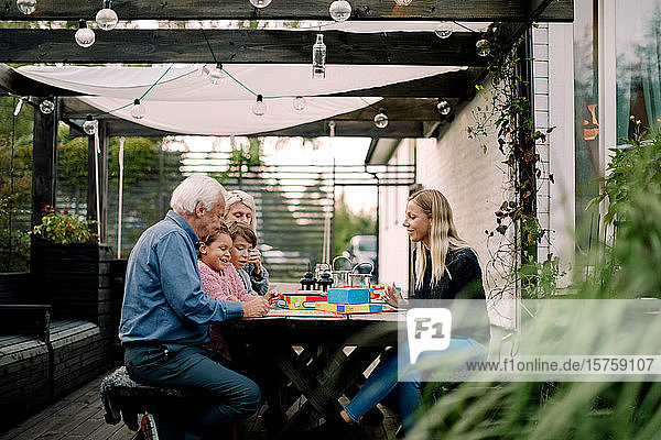 Smiling family playing board game while sitting at table in patio