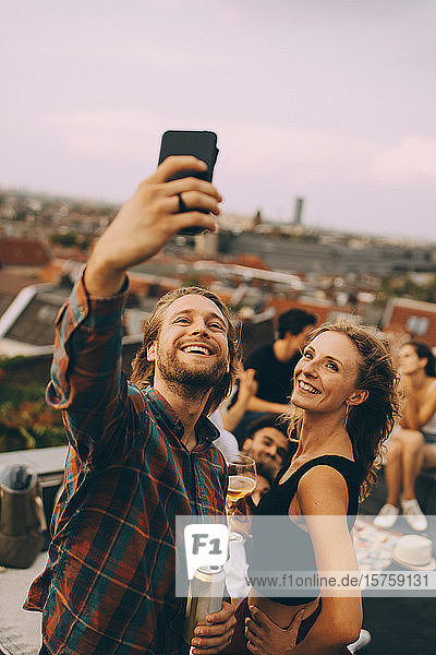 Glücklicher Mann nimmt sich mit fröhlichen Freunden während einer Dachparty auf der Terrasse