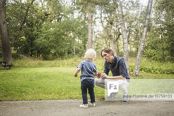 Vater und Sohn mit Spielzeugauto auf Fußweg gegen Pflanzen im Park