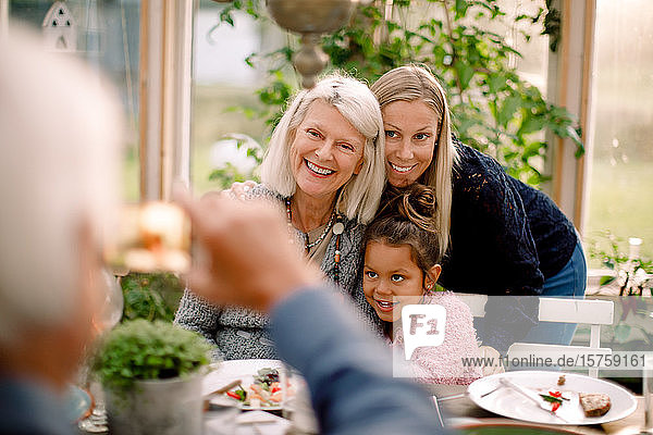 Älterer Mann fotografiert lächelnde Familie mit Mobiltelefon während des Mittagessens