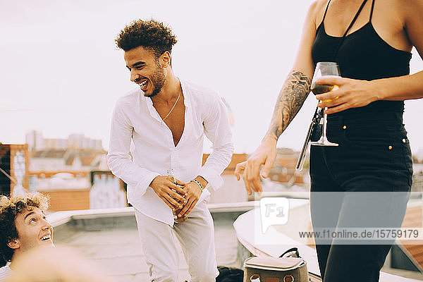 Fröhlicher junger Mann tanzt und trinkt bei einer Party mit Freunden auf der Terrasse