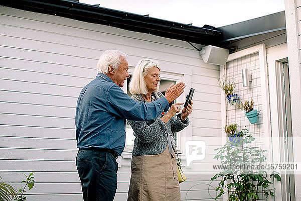 Älterer Mann spricht mit Frau  die ein Mobiltelefon gegen ihr Haus hält
