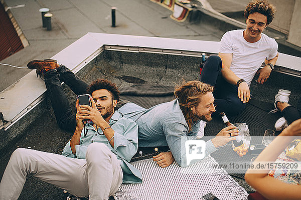 Man texting on mobile phone while friends enjoying beer on terrace at party