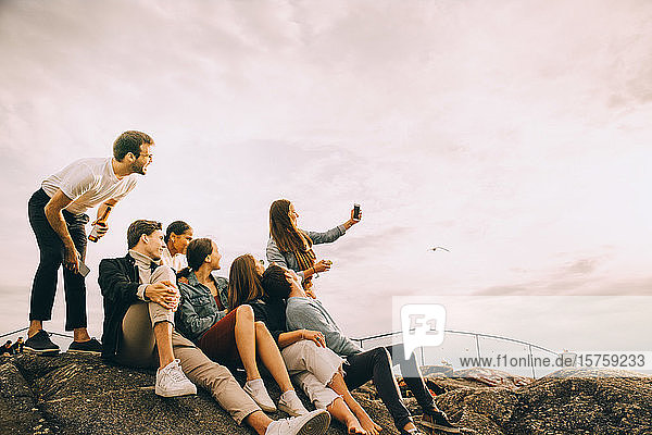Woman taking selfie with friends on rock formation against sky in picnic