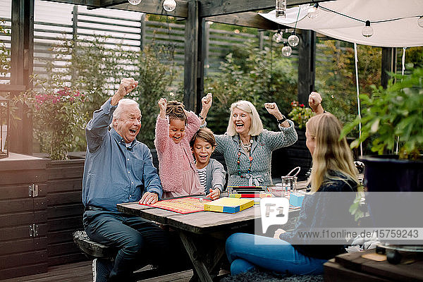 Fröhliche Familie spielt Brettspiel  während sie im Hinterhof am Tisch sitzt