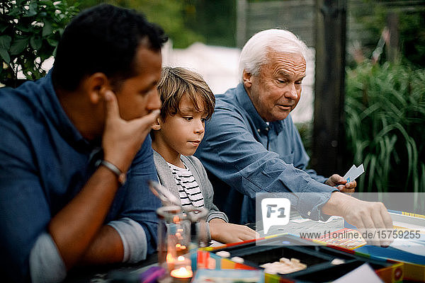 Mehrgenerationen-Familie spielt Brettspiel  während sie im Hinterhof am Tisch sitzt