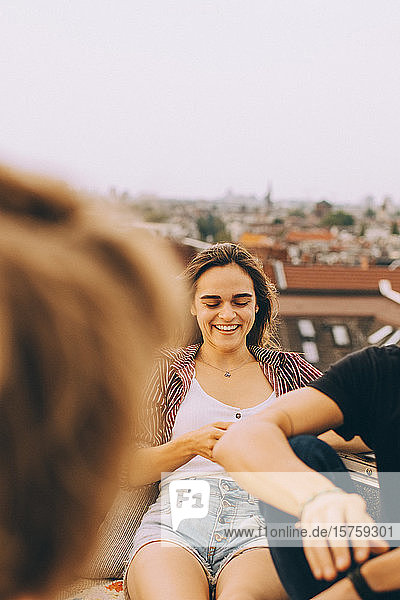 Lächelnde junge Frau amüsiert sich mit Freunden auf der Terrasse bei einer Dachfeier