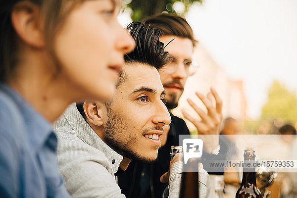 Smiling man sitting by male and female friend at social gathering