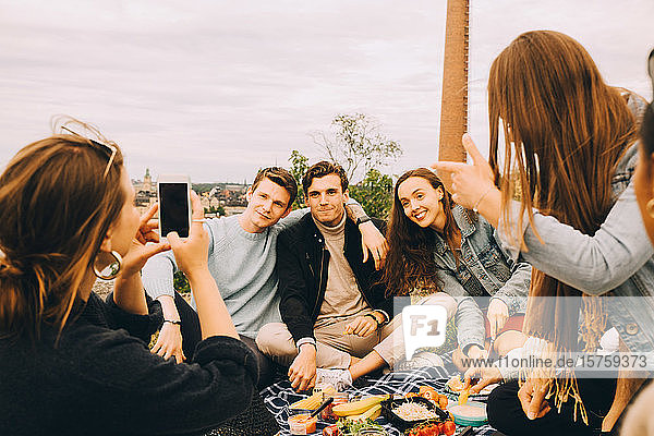 Frau fotografiert Freunde beim gemeinsamen Picknick gegen den Himmel