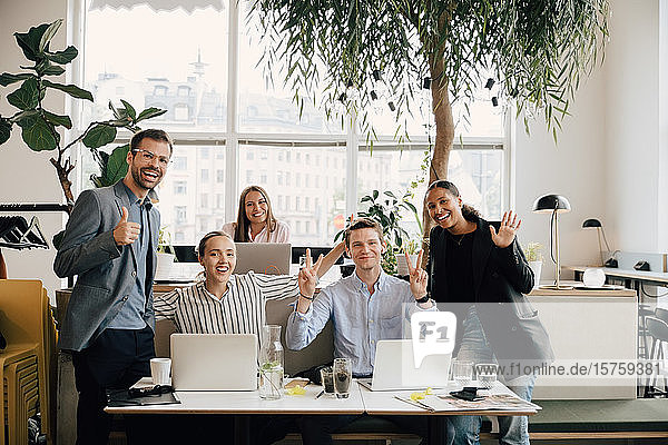 Porträt von lächelnden Kollegen mit Laptops  die am Schreibtisch im Coworking Space gestikulieren