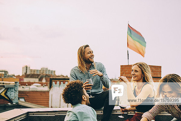 Fröhliche Freunde unterhalten sich beim gemeinsamen Weingenuss auf der Terrasse während einer Party gegen den Himmel