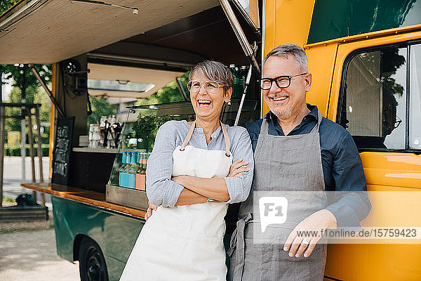 Happy mature couple looking away while standing against food truck