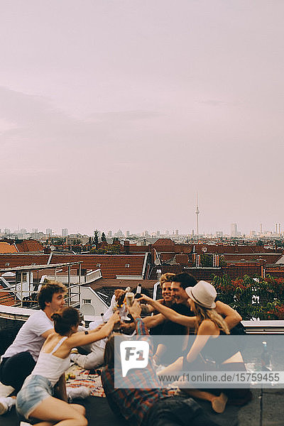 Männliche und weibliche Freunde stoßen auf Bier an  während sie sich auf einer Terrasse in der Stadt entspannen