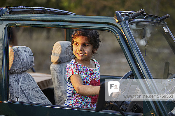 Kleines Mädchen hinter den Rädern eines Fahrzeugs