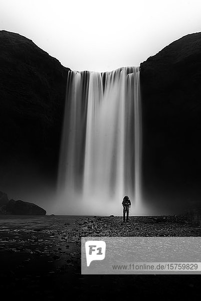 Tourist steht und schaut zum Wasserfall hinauf  Island