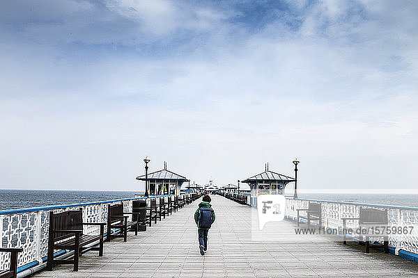 Junge  der an einem Pier am Meer spazieren geht.