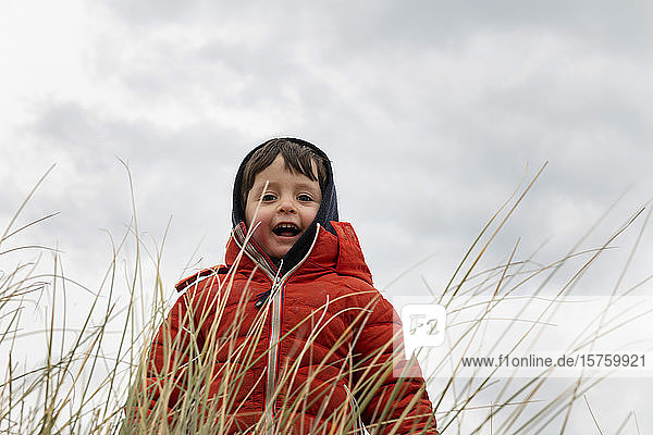 Junge in roter Kugelfischjacke hinter langem Gras