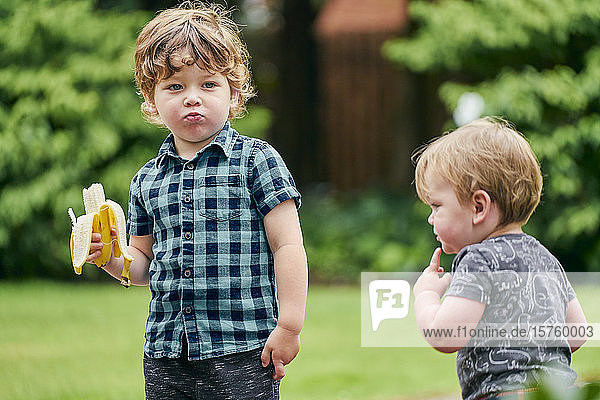 Kleinkinder erkunden und essen Banane im Park