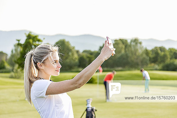 Woman taking selfie on golf course  friends playing golf in background
