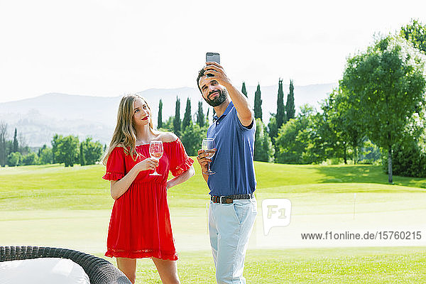Paar mit Weingläsern beim Selfie auf dem Golfplatz