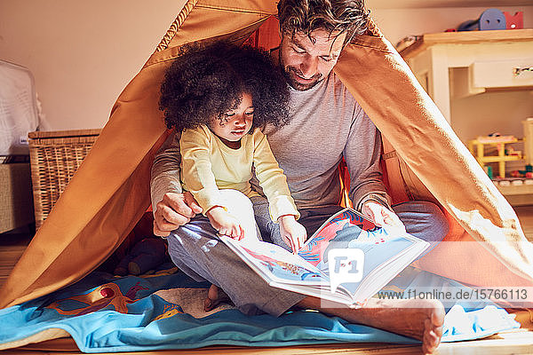 Vater und Tochter lesen ein Buch im Tipi
