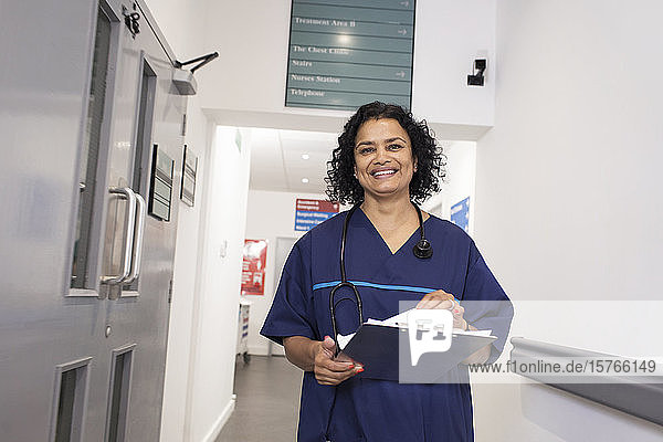 Porträt einer lächelnden  selbstbewussten Ärztin mit Krankenblatt bei der Visite im Krankenhausflur