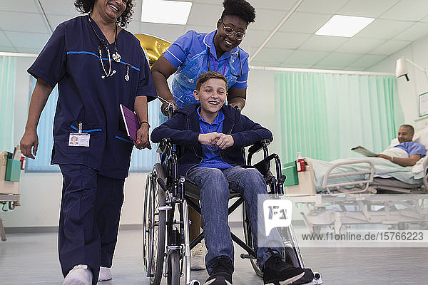 Arzt und Krankenschwester schieben einen Jungen im Rollstuhl auf der Krankenstation