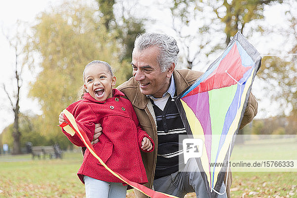 Playful grandfather and granddaughter flying a kite in autumn park