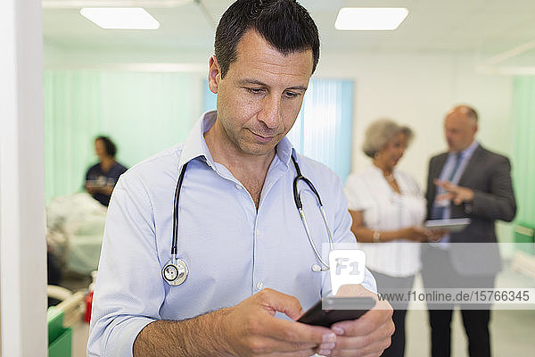 Männlicher Arzt  der ein Smartphone in einer Krankenstation benutzt