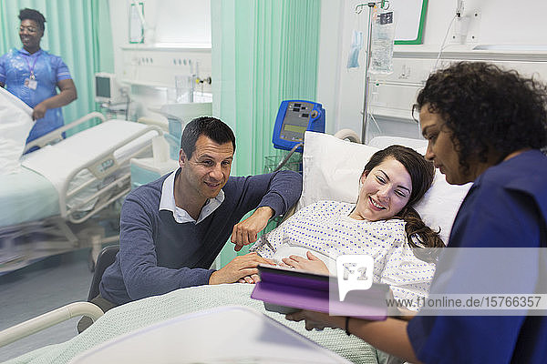 Arzt mit digitalem Tablet bei der Visite  im Gespräch mit einem Paar auf der Krankenstation