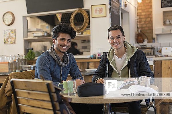 Portrait confident young male college students studying at cafe table