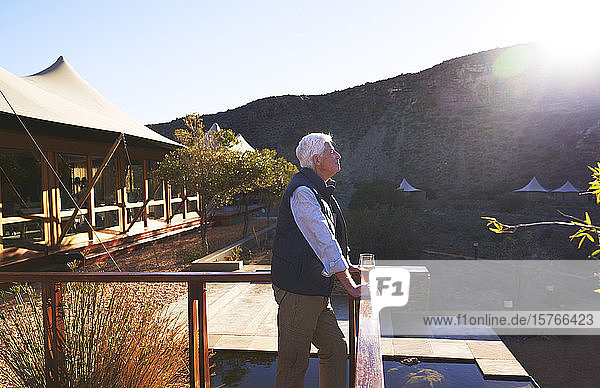 Gelassener älterer Mann entspannt sich auf dem sonnigen Balkon einer Safari-Lodge