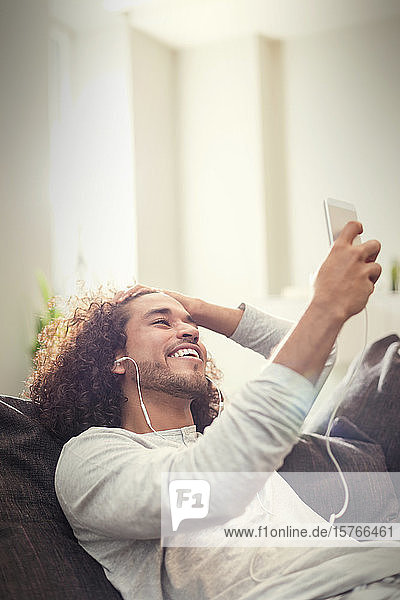 Glücklicher junger Mann  der mit Kopfhörern und mp3-Player auf dem Sofa Musik hört