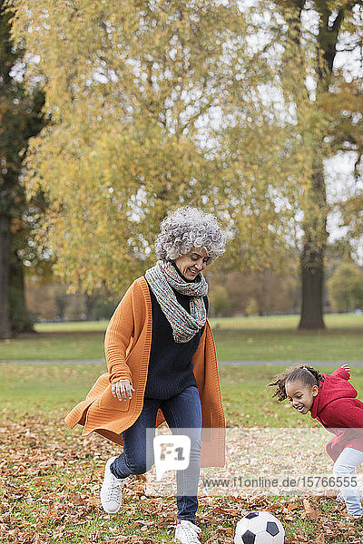Verspielte Großmutter spielt Fußball mit Enkelin im Herbst Park