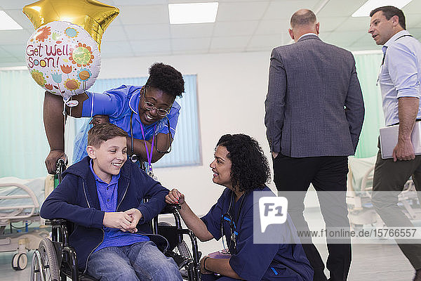 Arzt und Krankenschwester im Gespräch mit einem jungen Patienten im Rollstuhl auf einer Krankenhausstation