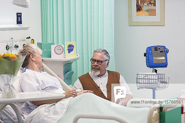 Zärtlicher älterer Mann  der seine Frau im Krankenhaus besucht und mit ihr spricht