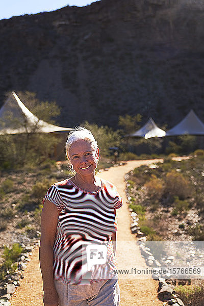 Porträt einer glücklichen älteren Frau auf dem Fußweg vor den Hütten einer Safari-Lodge