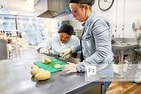 Koch und junge Frau mit Down-Syndrom beim Kartoffelschneiden in einem Café