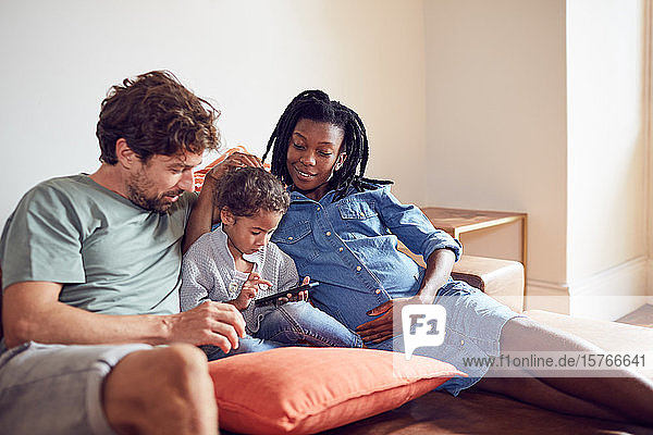 Young pregnant family using smart phone on living room sofa