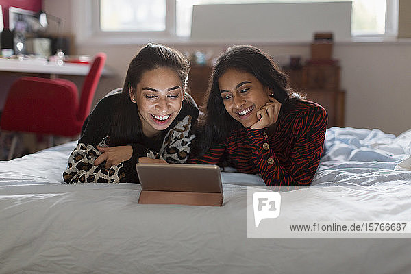 Glückliche Mädchen im Teenageralter benutzen ein digitales Tablet auf dem Bett