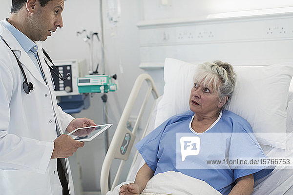Arzt mit digitalem Tablet bei der Visite  Gespräch mit älterem Patienten im Krankenhausbett